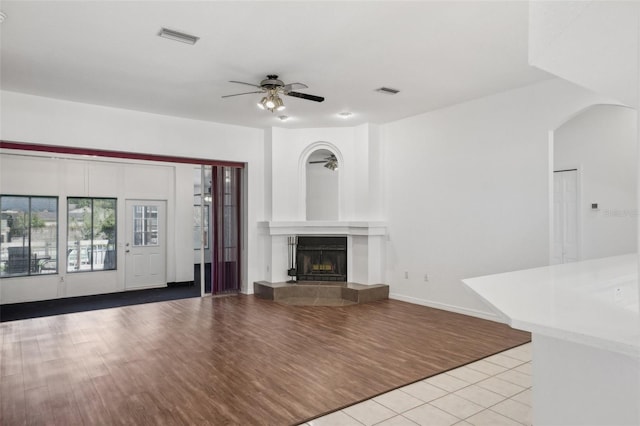 unfurnished living room with a tile fireplace, ceiling fan, and light hardwood / wood-style floors