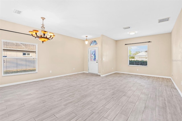 empty room with light hardwood / wood-style floors and an inviting chandelier