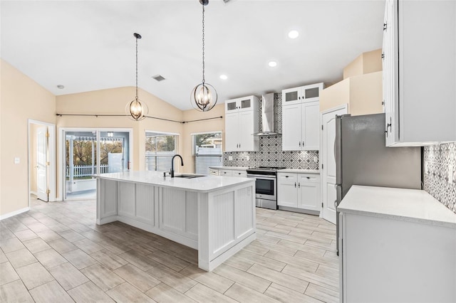 kitchen with a kitchen island with sink, white cabinets, vaulted ceiling, wall chimney exhaust hood, and stainless steel range oven