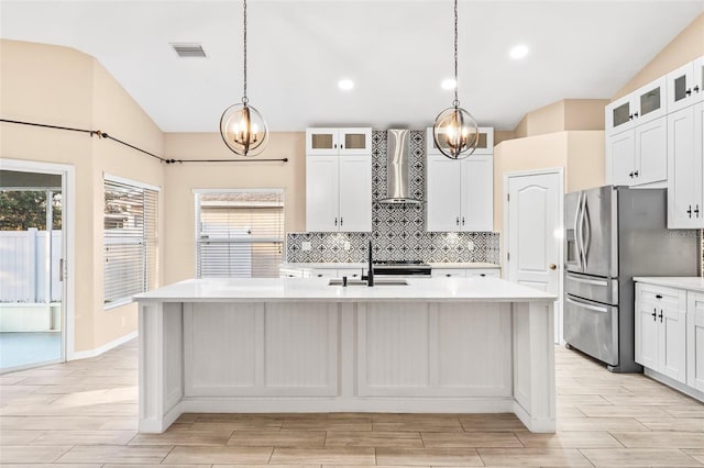 kitchen featuring vaulted ceiling, a center island with sink, white cabinets, and wall chimney range hood