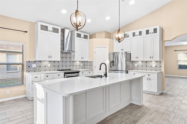 kitchen with white cabinets, appliances with stainless steel finishes, a kitchen island with sink, and wall chimney exhaust hood