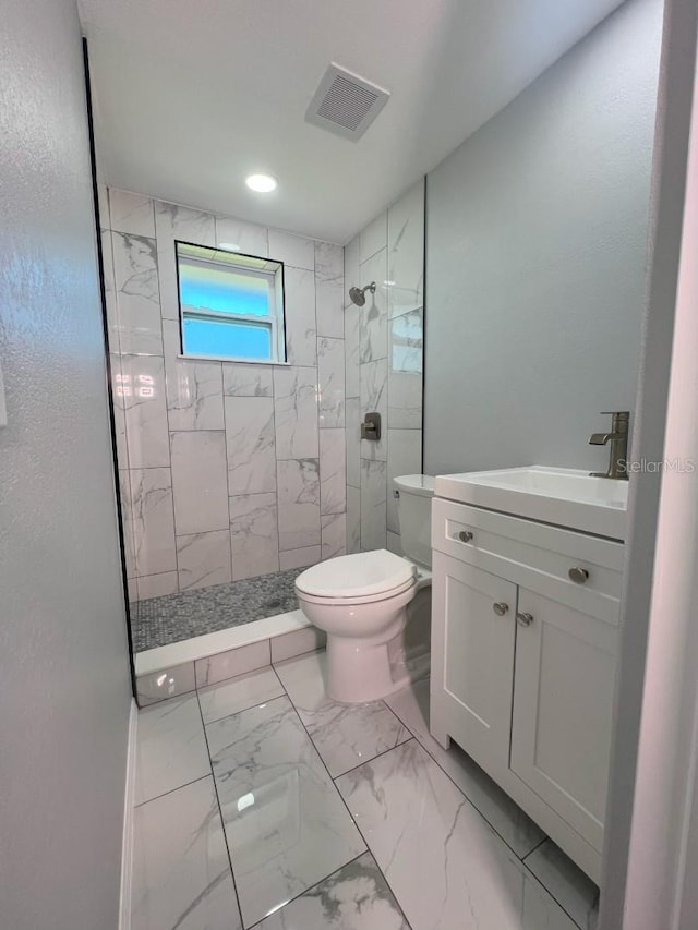 bathroom with tiled shower, vanity, and toilet