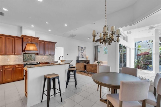 kitchen with a kitchen bar, backsplash, custom exhaust hood, stainless steel range with electric cooktop, and an island with sink