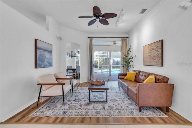 living room with ceiling fan, wood-type flooring, track lighting, and ornamental molding