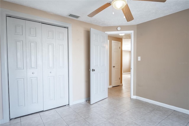 unfurnished bedroom featuring ceiling fan, light tile patterned flooring, a textured ceiling, and a closet