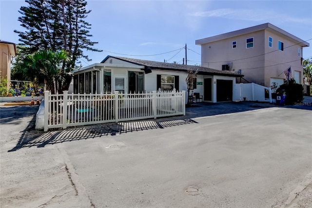 view of front facade with aphalt driveway, a fenced front yard, an attached garage, and a sunroom