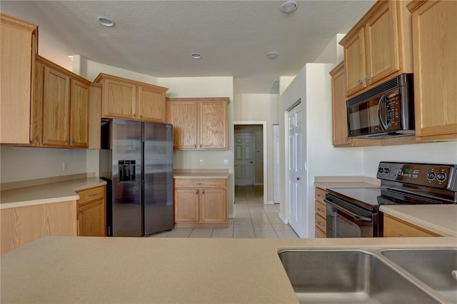 kitchen with black appliances, light tile patterned flooring, sink, and a textured ceiling