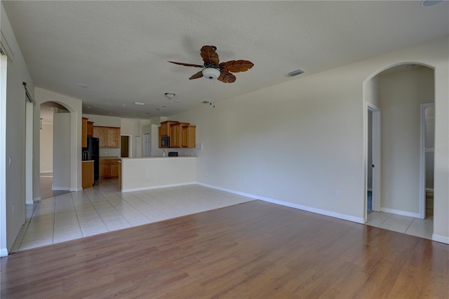 unfurnished living room with ceiling fan, a textured ceiling, and light hardwood / wood-style flooring