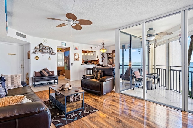 living room with a textured ceiling, light wood-type flooring, and a wall of windows