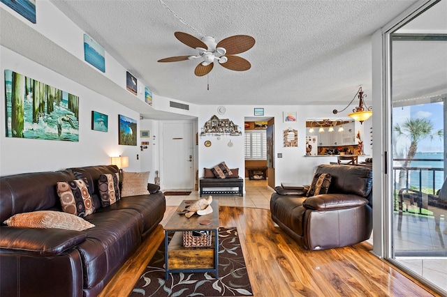 living room with hardwood / wood-style flooring, ceiling fan, a water view, and a textured ceiling