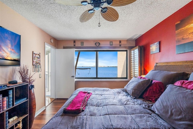 bedroom with a textured ceiling, a water view, ceiling fan, and hardwood / wood-style flooring