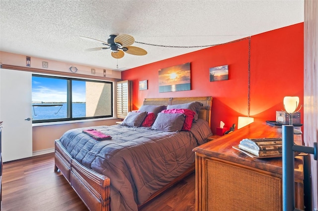 bedroom with a textured ceiling, dark hardwood / wood-style flooring, a water view, and ceiling fan