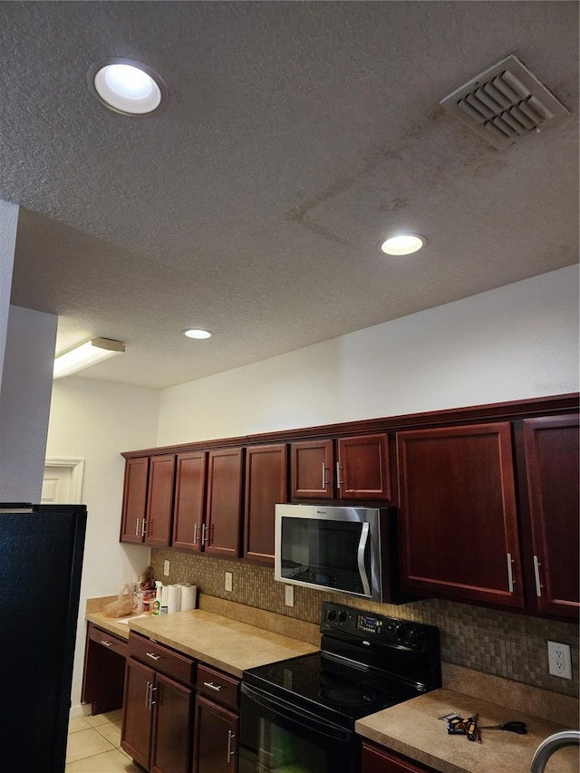 kitchen featuring backsplash, light tile patterned flooring, black appliances, and a textured ceiling