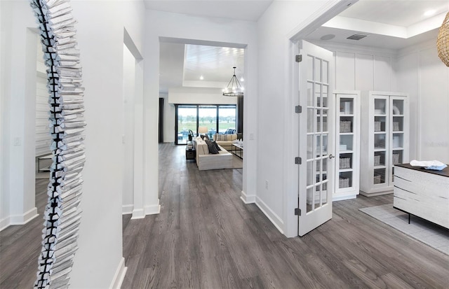 corridor featuring dark hardwood / wood-style floors, a raised ceiling, and an inviting chandelier