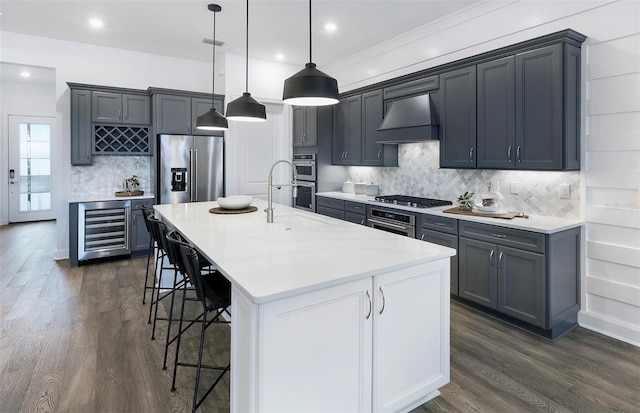 kitchen featuring pendant lighting, premium range hood, a center island with sink, wine cooler, and appliances with stainless steel finishes