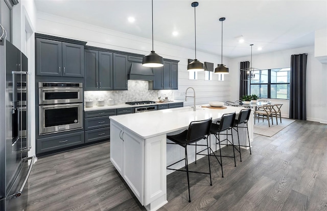 kitchen with a kitchen breakfast bar, dark hardwood / wood-style flooring, stainless steel appliances, pendant lighting, and a center island with sink