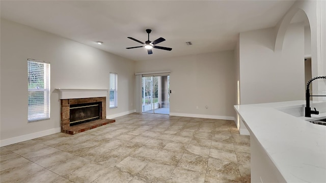 unfurnished living room with ceiling fan, a fireplace, and sink