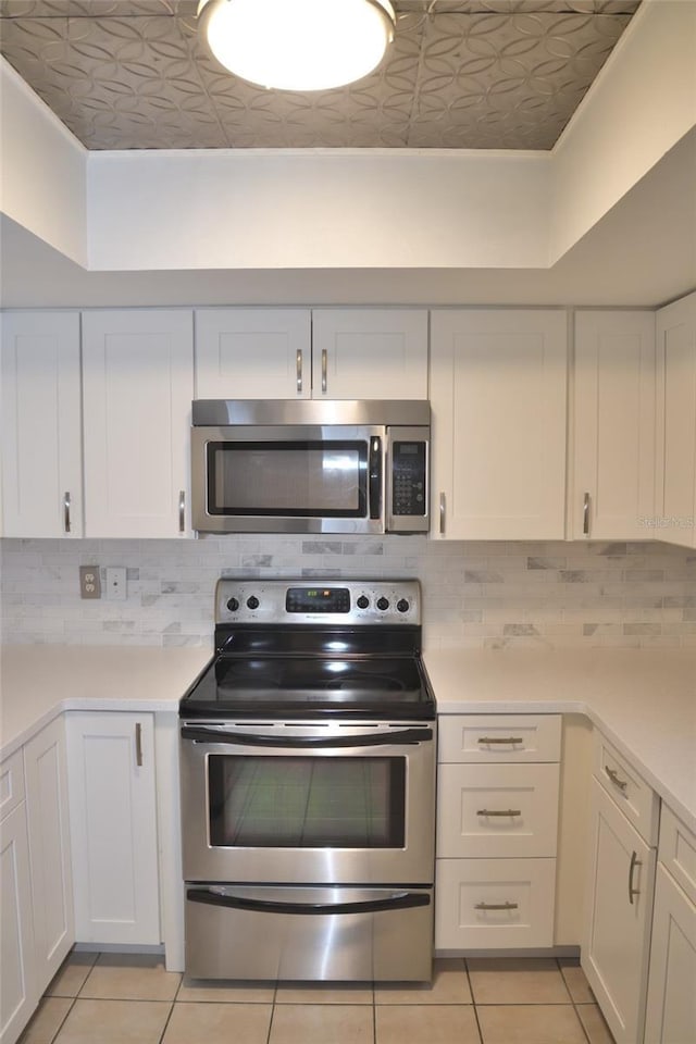 kitchen with stainless steel appliances, light tile patterned floors, white cabinets, and tasteful backsplash