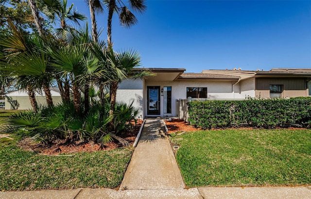 view of front of house with stucco siding, a front lawn, and fence