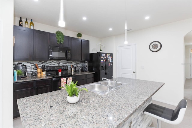 kitchen featuring decorative light fixtures, sink, black appliances, and a center island with sink