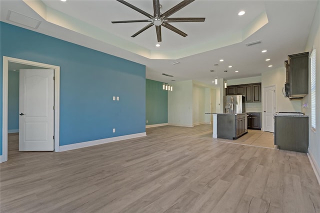 unfurnished living room with ceiling fan, light hardwood / wood-style floors, and a raised ceiling