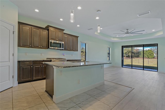 kitchen with light stone counters, stainless steel appliances, ceiling fan, sink, and an island with sink