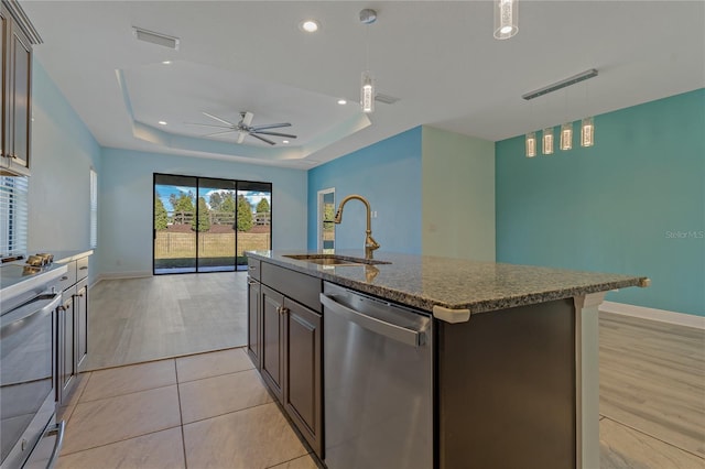 kitchen with a tray ceiling, sink, appliances with stainless steel finishes, and an island with sink