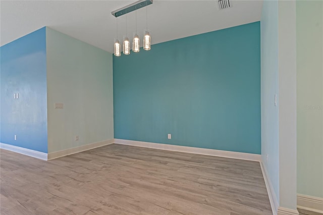 spare room featuring a chandelier and light hardwood / wood-style flooring