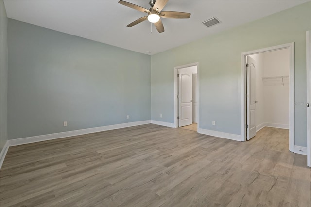 unfurnished bedroom featuring ceiling fan, a closet, a spacious closet, and light wood-type flooring