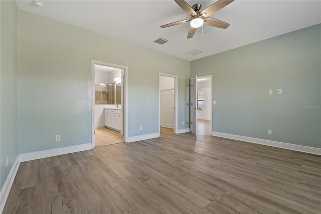 unfurnished bedroom with light wood-type flooring, a spacious closet, ceiling fan, and connected bathroom