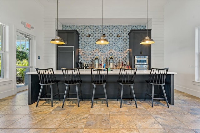 kitchen featuring paneled fridge, a breakfast bar, hanging light fixtures, and an island with sink