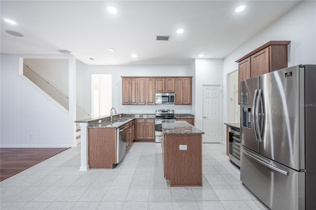 kitchen with dark stone counters, a kitchen island, light hardwood / wood-style floors, kitchen peninsula, and stainless steel appliances