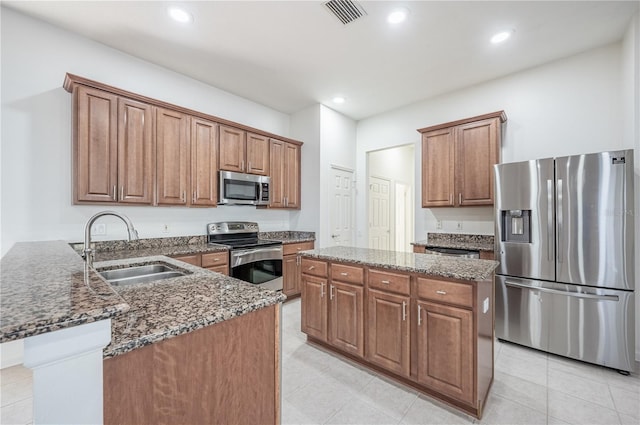 kitchen with dark stone counters, sink, light tile patterned flooring, kitchen peninsula, and stainless steel appliances