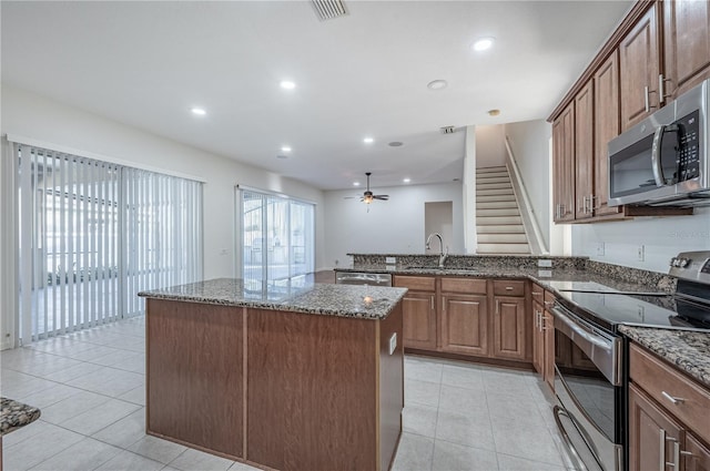 kitchen featuring ceiling fan, sink, stainless steel appliances, dark stone countertops, and a kitchen island