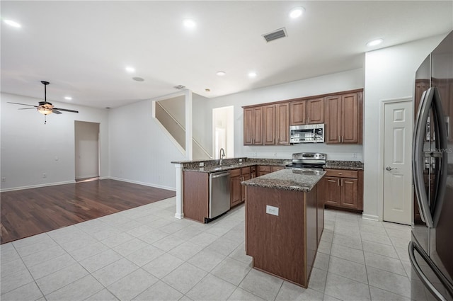 kitchen with dark stone counters, stainless steel appliances, ceiling fan, light hardwood / wood-style flooring, and a kitchen island