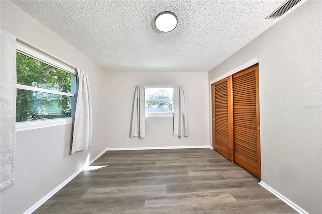 unfurnished bedroom with a textured ceiling, a closet, and dark hardwood / wood-style floors