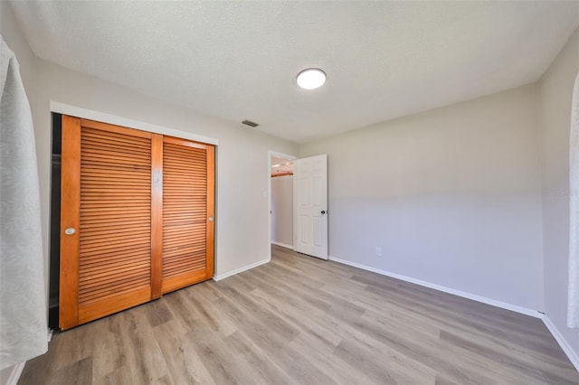 unfurnished bedroom with light wood-type flooring, a textured ceiling, and a closet