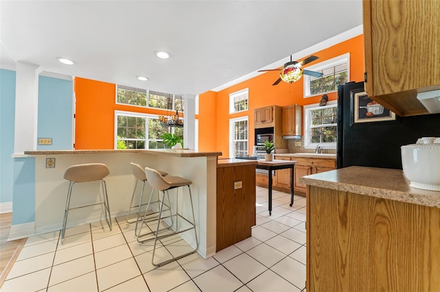 kitchen with a kitchen bar, kitchen peninsula, ceiling fan, crown molding, and light tile patterned floors