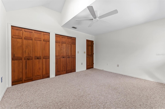 unfurnished bedroom with carpet flooring, ceiling fan, lofted ceiling, and two closets