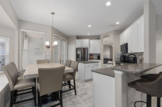 kitchen with white cabinets, decorative light fixtures, a kitchen breakfast bar, and black appliances