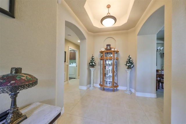 foyer entrance featuring a tray ceiling, light tile patterned flooring, a textured ceiling, and washer / dryer