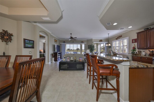 kitchen featuring ceiling fan, crown molding, dark stone counters, decorative light fixtures, and a breakfast bar area