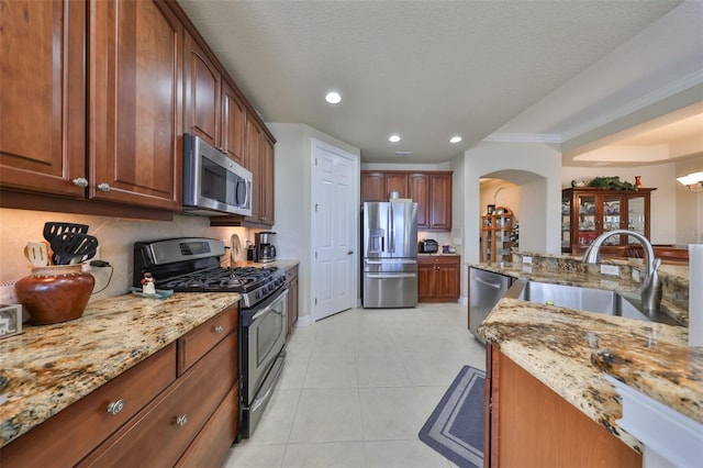 kitchen featuring light stone countertops, appliances with stainless steel finishes, ornamental molding, a textured ceiling, and sink