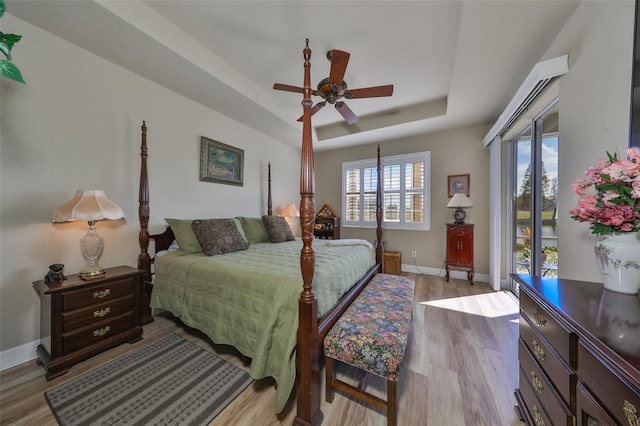 bedroom with light wood-type flooring, a tray ceiling, and ceiling fan