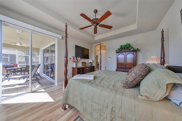 bedroom with access to exterior, light wood-type flooring, a tray ceiling, and ceiling fan