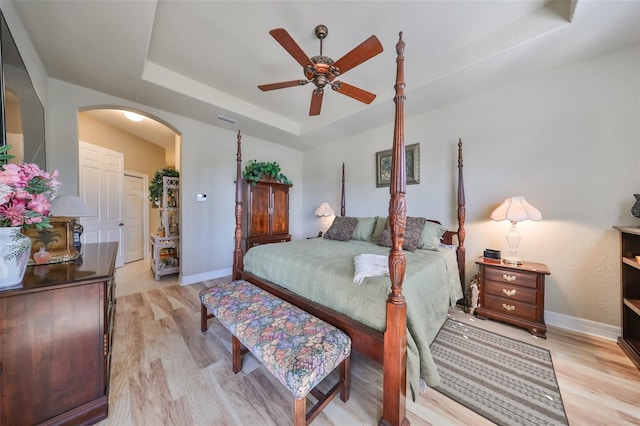 bedroom featuring light hardwood / wood-style floors, ceiling fan, and a tray ceiling