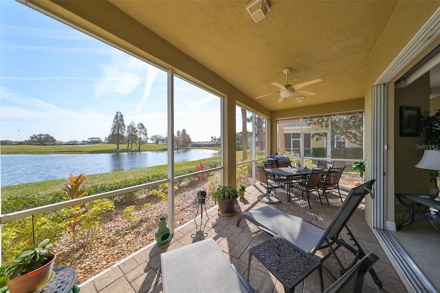 sunroom with ceiling fan and a water view