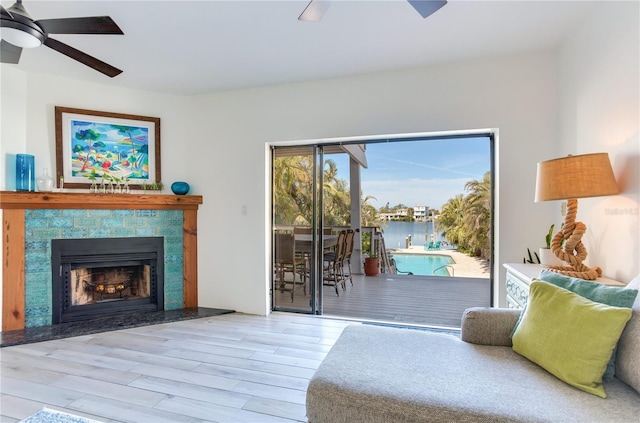 living room featuring ceiling fan, light wood-type flooring, and a tiled fireplace