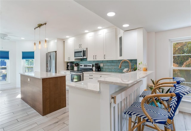 kitchen with pendant lighting, kitchen peninsula, light wood-type flooring, appliances with stainless steel finishes, and white cabinetry