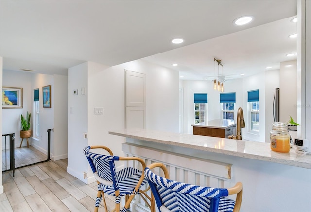 kitchen with sink, light stone counters, kitchen peninsula, pendant lighting, and light hardwood / wood-style floors